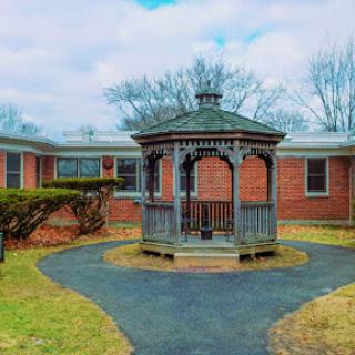 A charming gazebo surrounded by a path and brick buildings under a cloudy sky.
