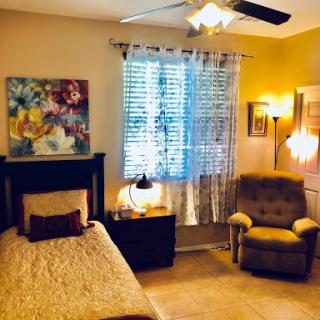 A cozy and well-lit bedroom featuring a comfortable bed, armchair, and colorful artwork.