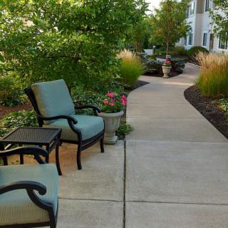 A serene outdoor patio area with cushioned chairs and a landscaped pathway surrounded by greenery.
