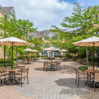 A charming outdoor patio area with tables, chairs, and umbrellas surrounded by lush greenery.