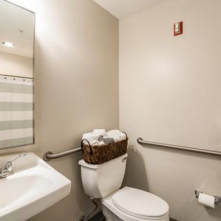 A clean, accessible bathroom with a sink, toilet, and mirror.