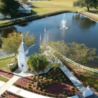 A scenic aerial view of a park featuring a pond with a central fountain, surrounded by pathways and lush greenery.