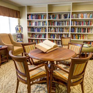 A cozy library with a round table surrounded by chairs, and bookshelves filled with books.