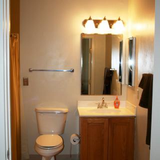 A small bathroom with a toilet, sink, mirror, and overhead light fixture.