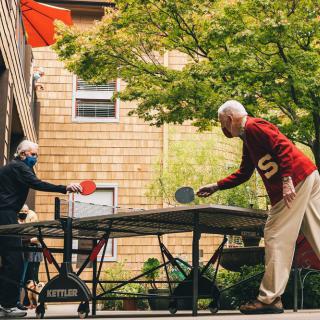 Two elderly individuals enjoying a game of table tennis outdoors.