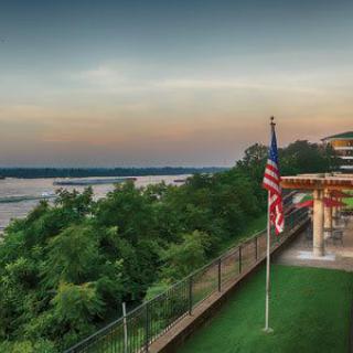A scenic view of a river at sunset with an American flag and a building overlooking lush greenery.