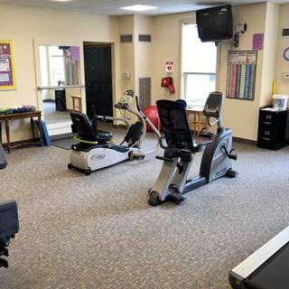 A small gym room equipped with exercise bikes, mirrors, and a TV screen.