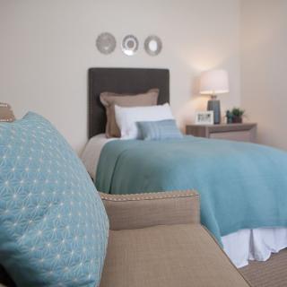 A cozy bedroom with a neatly made bed featuring a blue blanket and decorative pillows, alongside a nightstand with a lamp.