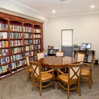 A cozy library reading area with a round table surrounded by chairs and shelves filled with books.