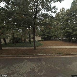 A suburban street view showing a house surrounded by trees.