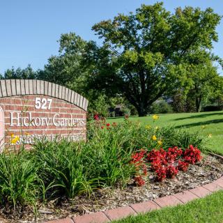 A brick sign with landscaping features vibrant flowers and lush greenery in a park setting.