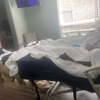 A patient resting in a hospital room, surrounded by medical equipment and comfort items.