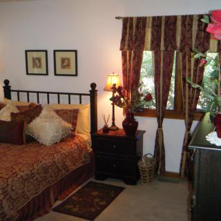 A cozy bedroom with elegant decor, featuring a bed, nightstand with a lamp, and a window with patterned curtains.