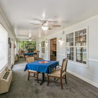 A cozy interior dining area with tables and chairs, featuring large windows and a ceiling fan.