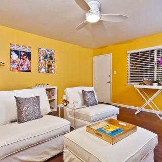 A cozy living room with yellow walls and white furniture, featuring modern decor and a ceiling fan.