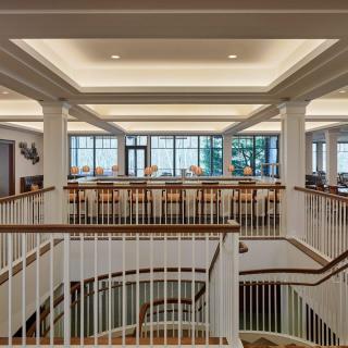 A spacious interior view of a library with a central staircase, surrounded by tables and large windows.