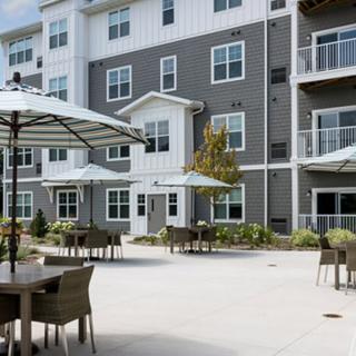 A modern apartment building with an outdoor patio featuring tables, chairs, and umbrellas.