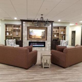 A cozy living room setup with sofas facing a fireplace, flanked by bookshelves and illuminated by a chandelier.