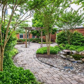 A beautifully landscaped garden with a winding stone pathway surrounded by lush greenery and trees.