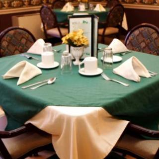 An elegantly set dining table in a restaurant with green and white tablecloths, neatly arranged napkins, cups, glasses, and cutlery.