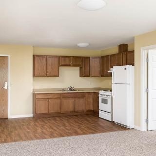A small, empty apartment kitchen with wooden cabinets and basic appliances.