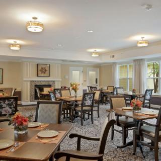 An elegant dining room with neatly arranged tables and chairs, featuring decorative flowers and warm lighting.