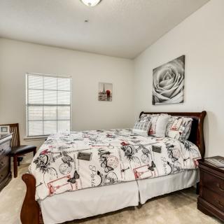 A cozy bedroom featuring a patterned bedspread, wooden furniture, and wall art.