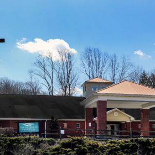 A church building with a prominent cross, surrounded by trees under a clear blue sky.