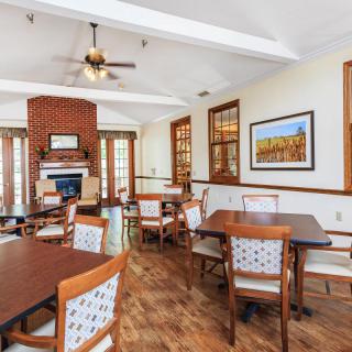 A cozy dining room with a brick fireplace, wooden floors, and neatly arranged tables and chairs.