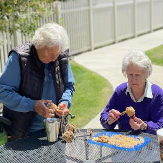 Two elderly women enjoying a sunny day outdoors while working on a cooking activity.