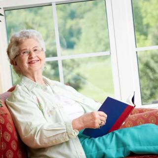 An elderly woman sitting by the window, enjoying a book.