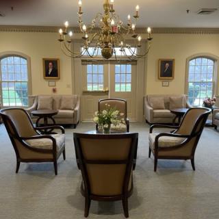 A well-appointed lounge with elegant furniture, featuring a chandelier and large windows.
