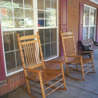 Two wooden rocking chairs on a porch beside large windows.