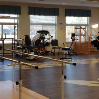 A spacious rehabilitation center equipped with various exercise machines and a barre for physical therapy.