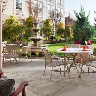 A serene outdoor patio with tables, chairs, and a garden featuring a fountain.