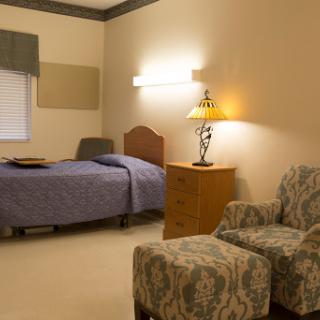 A cozy bedroom featuring a single bed, a bedside lamp, and comfortable seating.