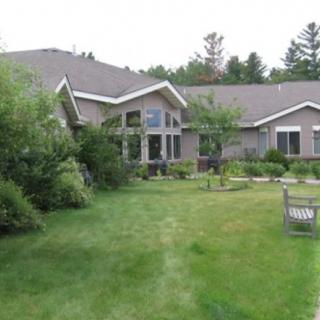 A house with a lush green yard and garden, featuring a real estate sign in the front.