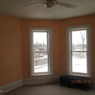 An empty room with two large windows and a ceiling fan, allowing natural light to fill the space.