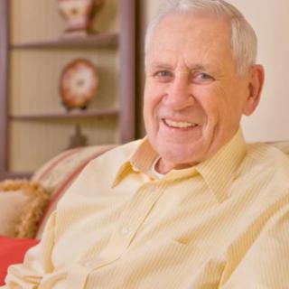 An elderly man sitting indoors, smiling warmly.