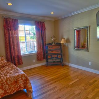A cozy bedroom with a bed, window with curtains, and hardwood floors.