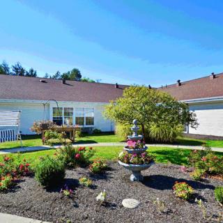 A sunny garden with a central fountain surrounded by a well-maintained lawn and plants in front of a house.