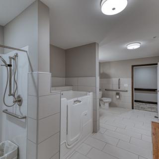 A spacious, accessible bathroom featuring a walk-in tub, shower, and safety grab bars.