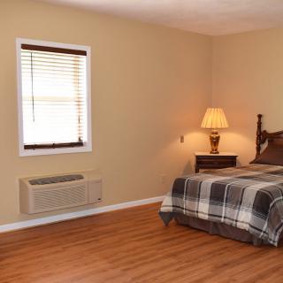 A cozy bedroom with a plaid bedspread, wooden floors, and a warm lamp.