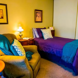 A cozy bedroom with a single bed, comfortable chair, and warm lighting.