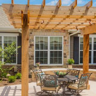 A cozy backyard patio with a wooden pergola, featuring a set of outdoor tables and chairs.
