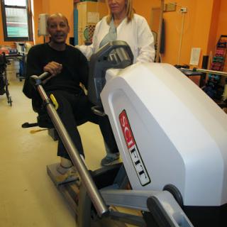 A person engaging in fitness activities on a rowing machine with assistance from a trainer.