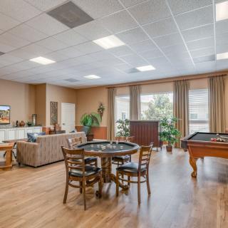 A spacious recreation room with a pool table, chairs around a card table, and comfortable seating by large windows.