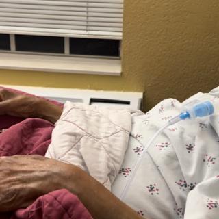 A patient resting in a hospital bed, covered with a quilt.