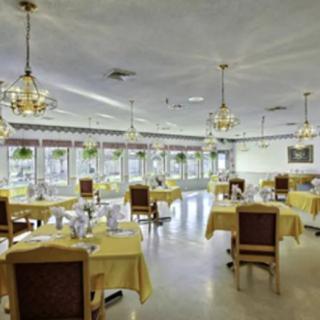 An elegant dining area with tables set for guests, featuring chandeliers and a warm atmosphere.