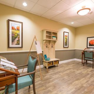 A cozy and well-decorated interior room with desks, chairs, and framed artwork on the walls.